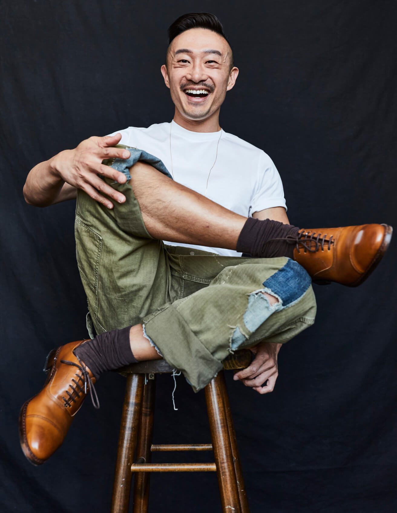 Steven Chu smiling in a white shirt, custom overalls, and oxford dress shoes